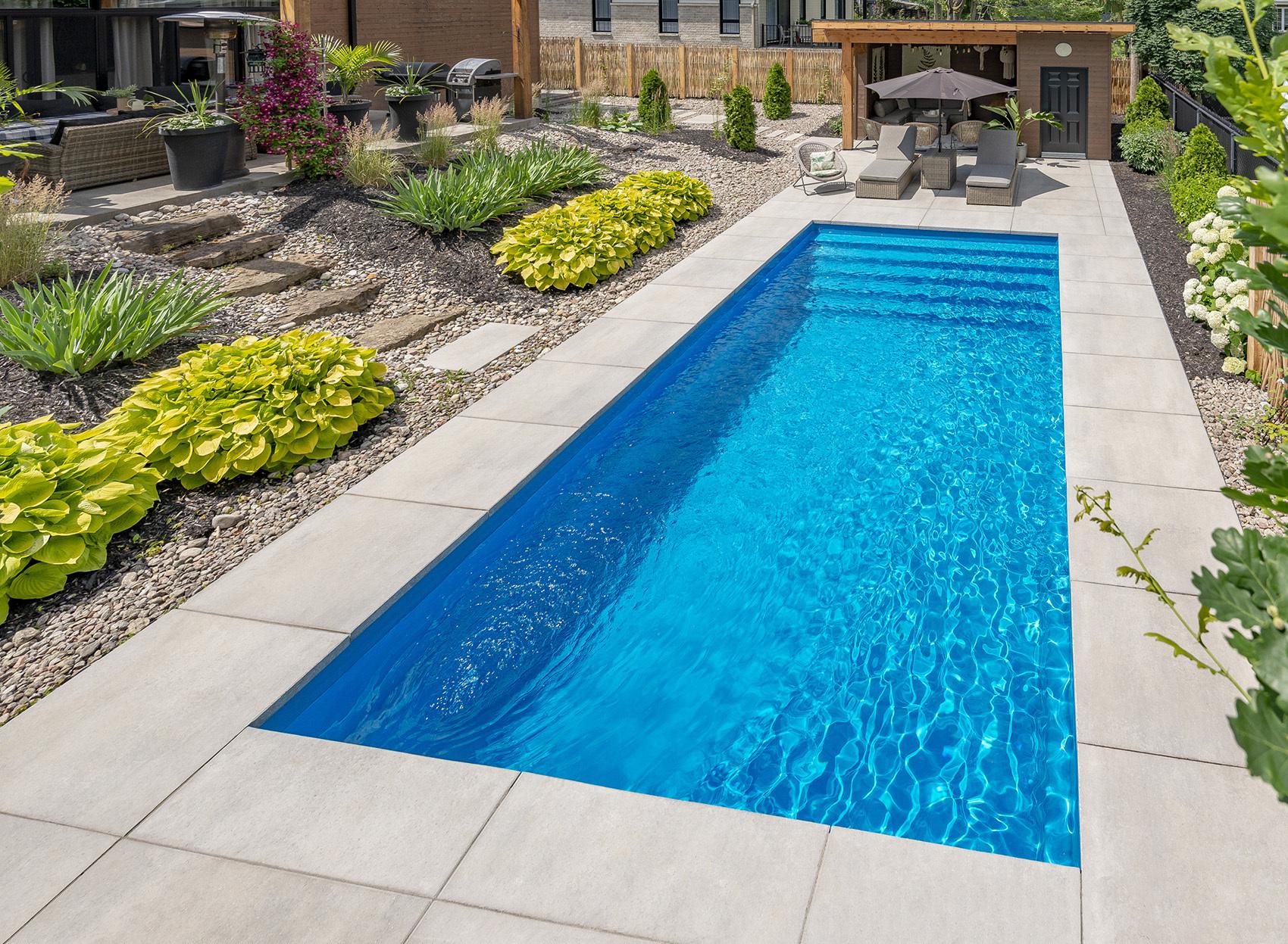 Modern fiberglass swimming pool with premium paving in a landscaped backyard